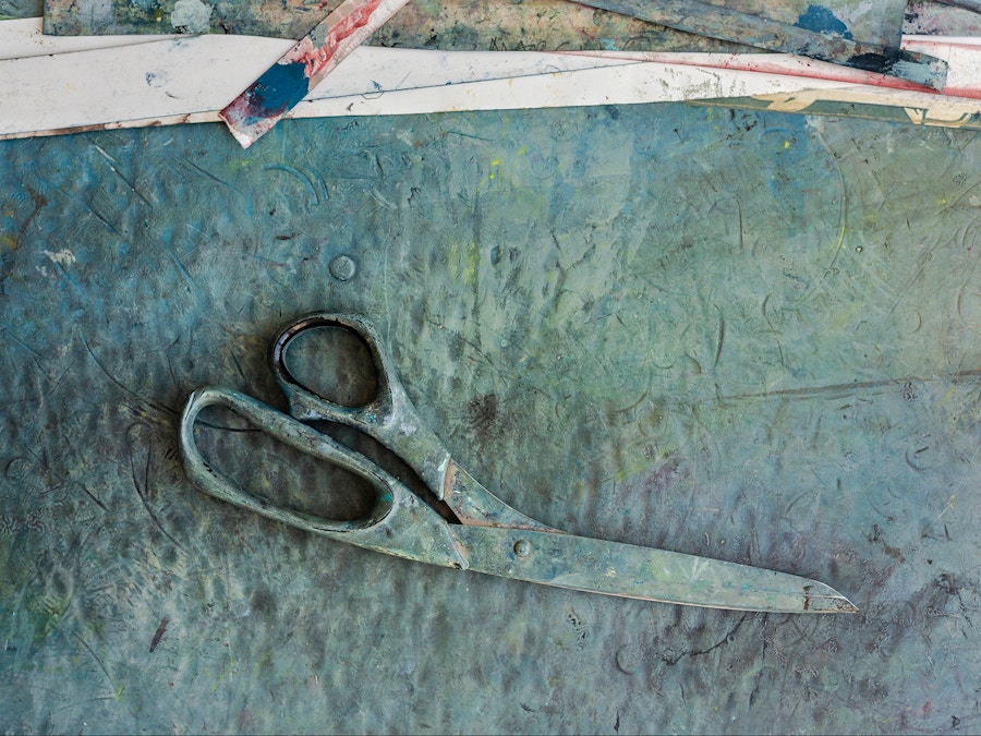 A pair of scissors covered in blue ink sit on an ink covered surface.
