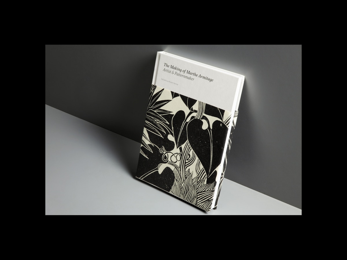 A book sits leaning against a dark grey background. The book has a black and cream patterned wrap-around cover on it.