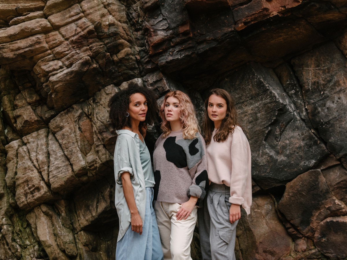 Three women standing close together in front of a rock face. They are all looking at the camera.