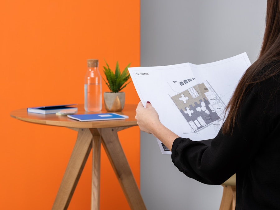 A women reading a floor plan. There is a wooden coffee table with a book and water carafe on it.