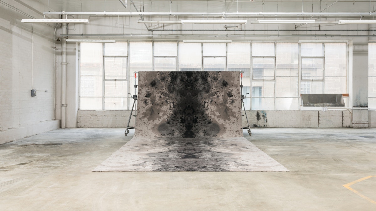 A large carpet swooping up from the floor onto a metal bar in front some windows.