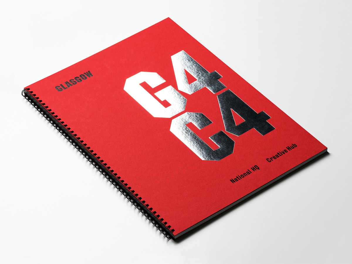 A red wire bound book that has silver foiled text on the front that reads "G4C4" sitting on a white surface.