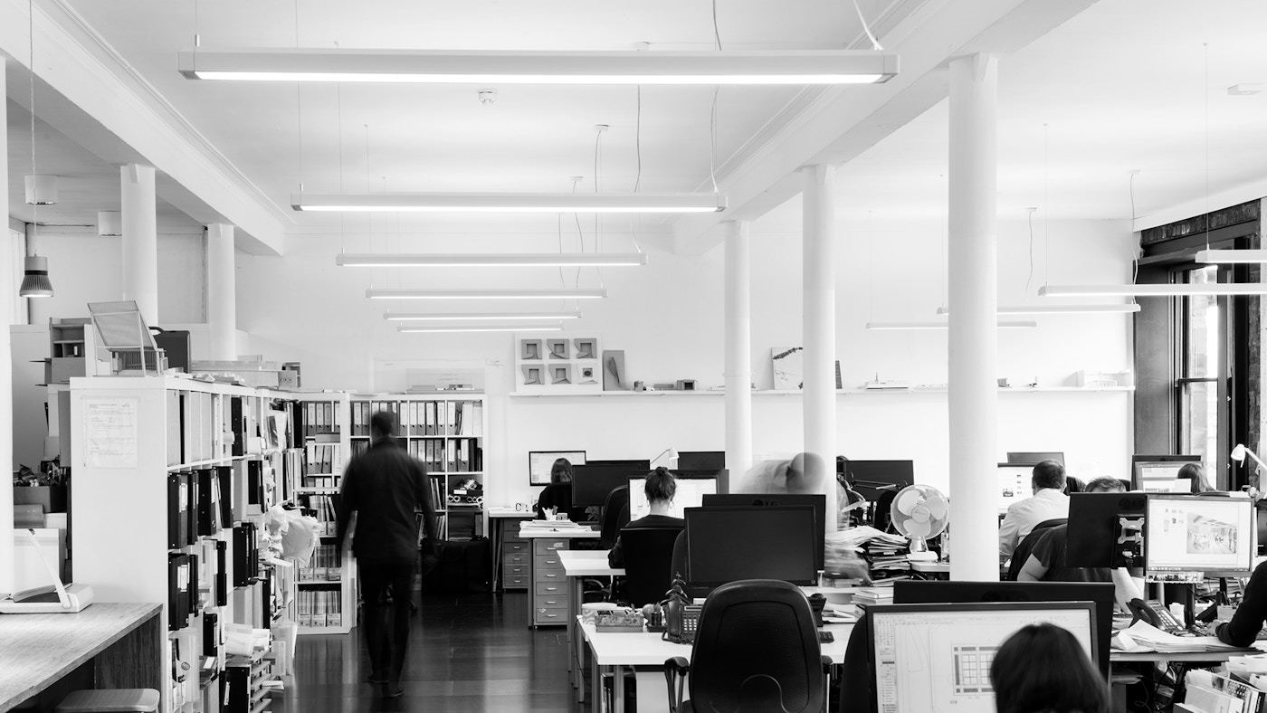 People sitting at office desks in a large open plan space. In black and white.