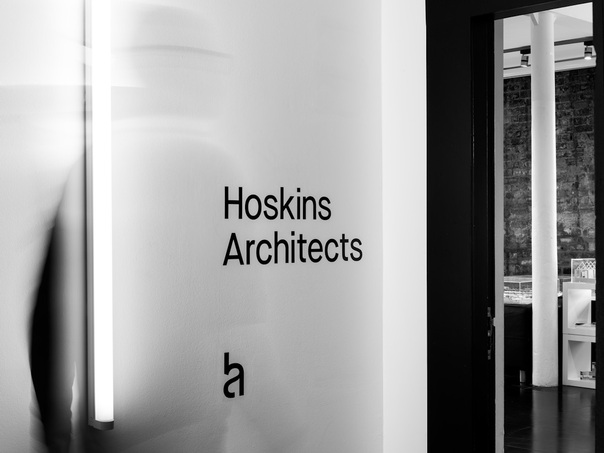Black vinyl lettering on a white wall that reads "Hoskins Architects". There is logo below the text.
