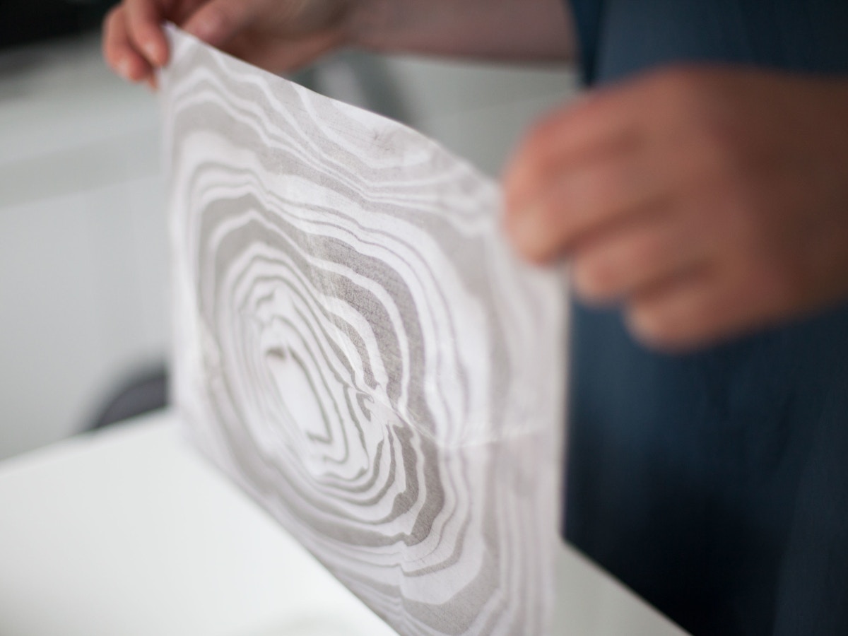 Two hands holding up a sheet of paper that has a swirled pattern on it.
