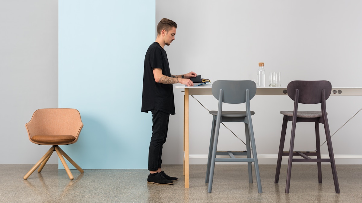 A man places objects onto a tall table. There are two barstools beside him.