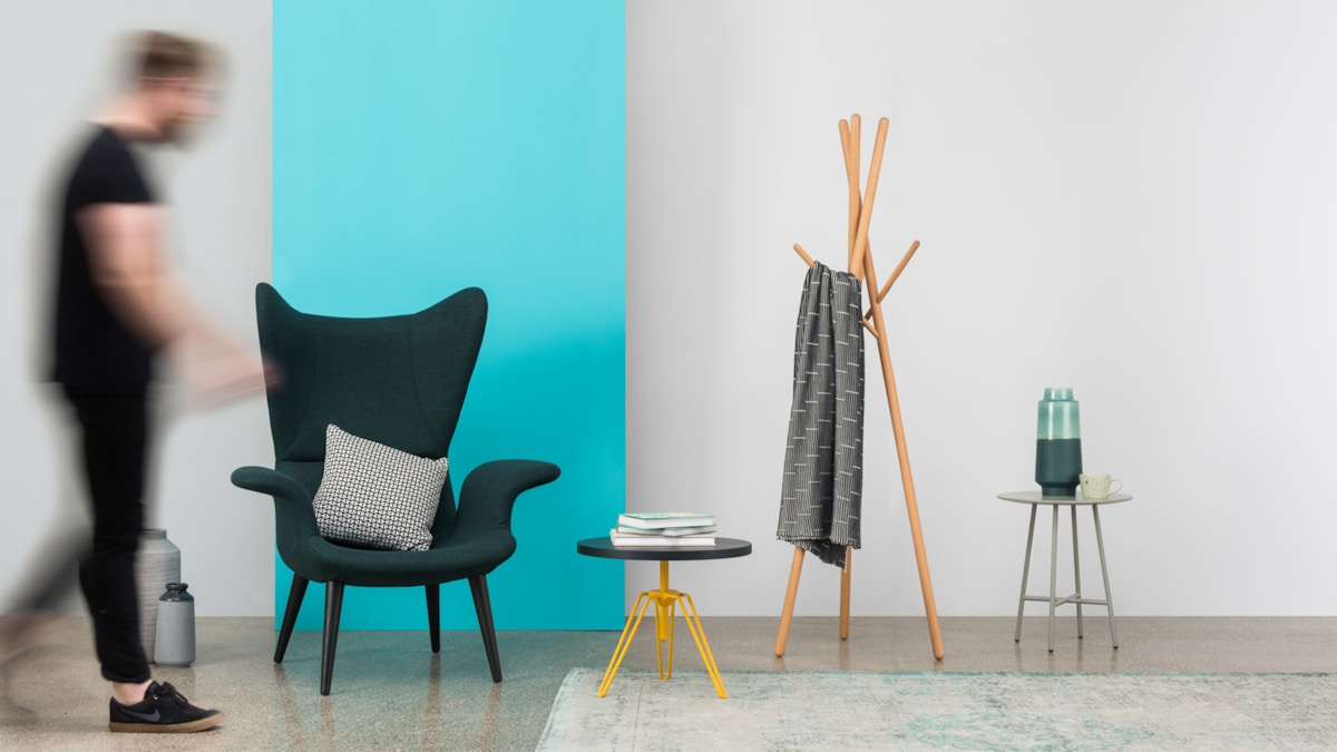 A set up of an armchair with coffee table and coat-rack beside.