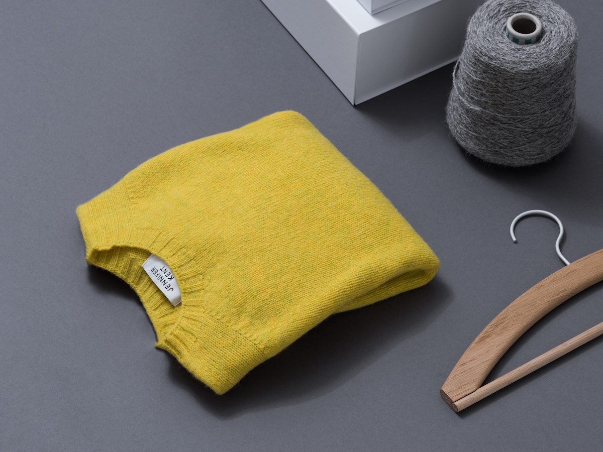 A yellow jumper siting with a wooden hanger and grey loom.