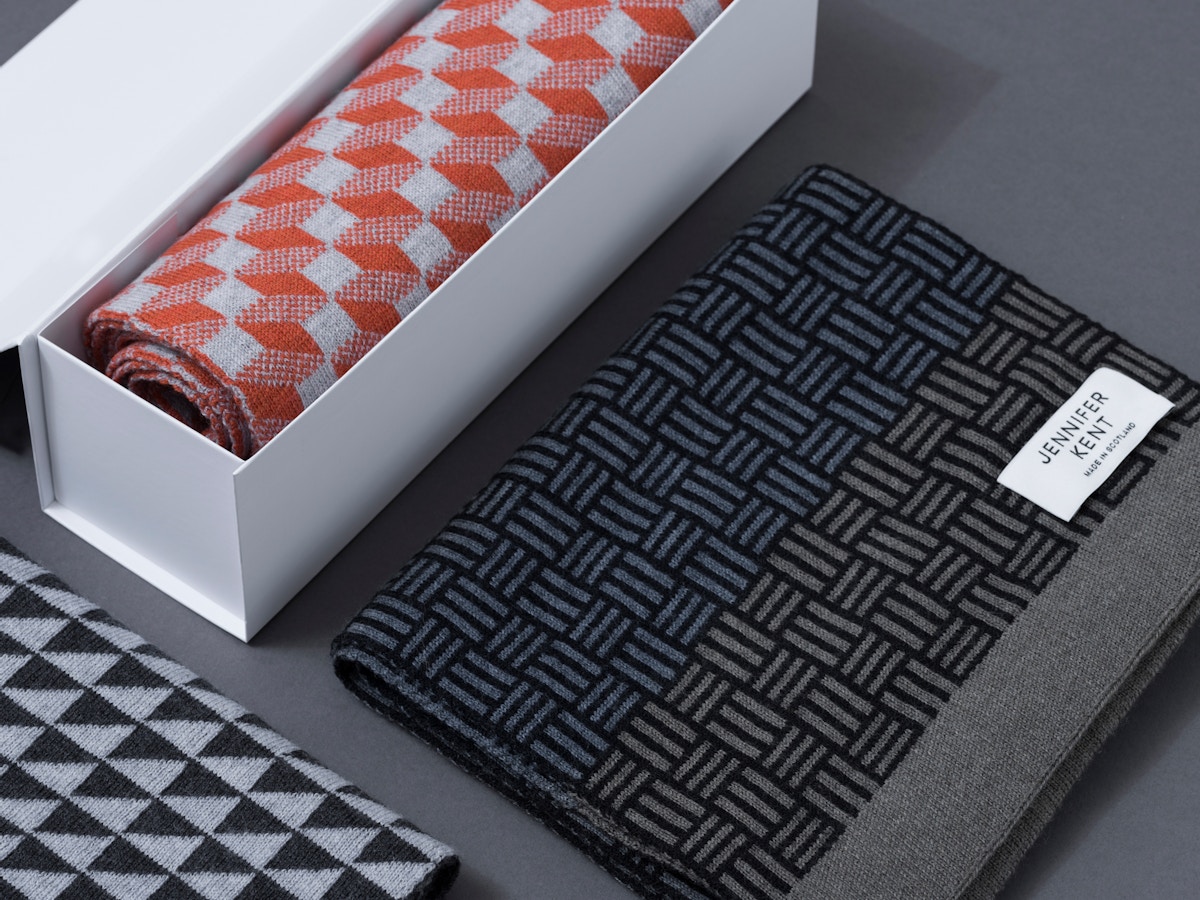 A white box with an orange patterned scarf sitting next to a black and grey patterned scarf.