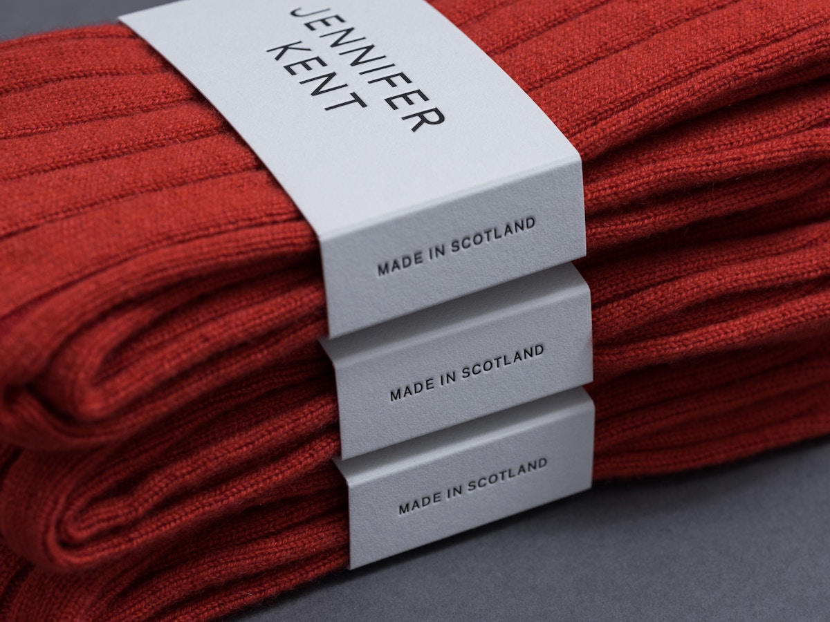 Detail of white packaging sleeve around a red pair of socks. There are three pairs stacked on top of each other.