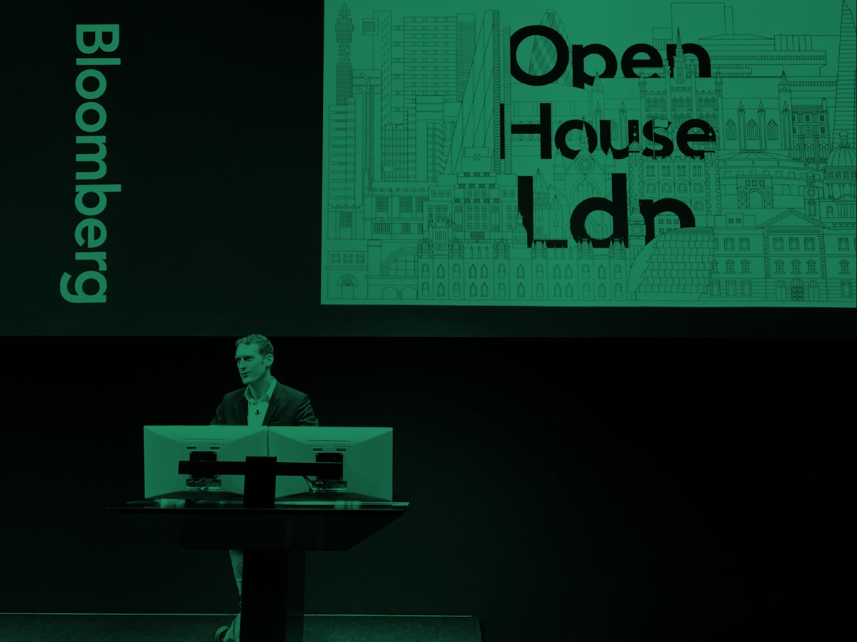 A man stands at a podium in front of a screen that has text on it. The photograph has been washed in green.