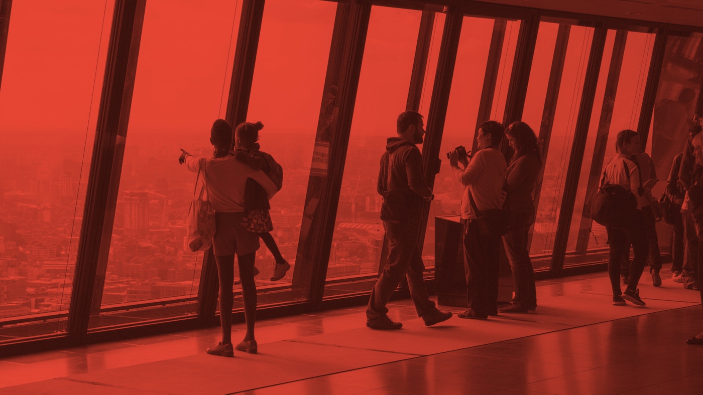 Groups of people standing at large windows looking out. The photograph has been washed in red.