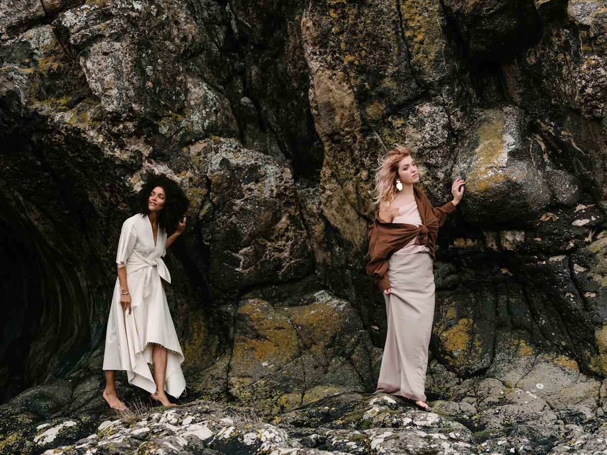 Two women standing barefoot on a cliff face.