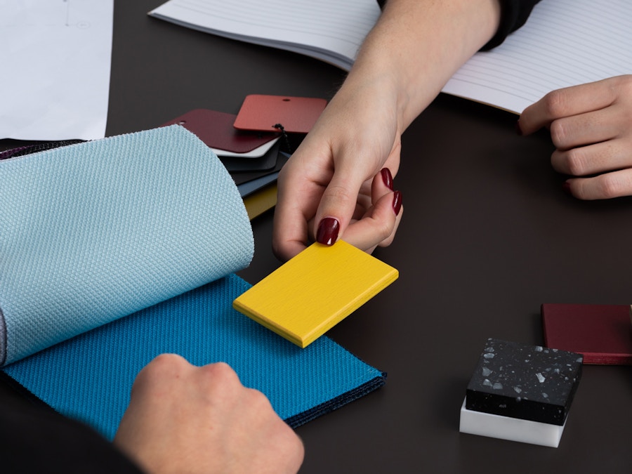 A close up of two pairs of hands comparing coloured swatches. There are other swatches on the table beside them.