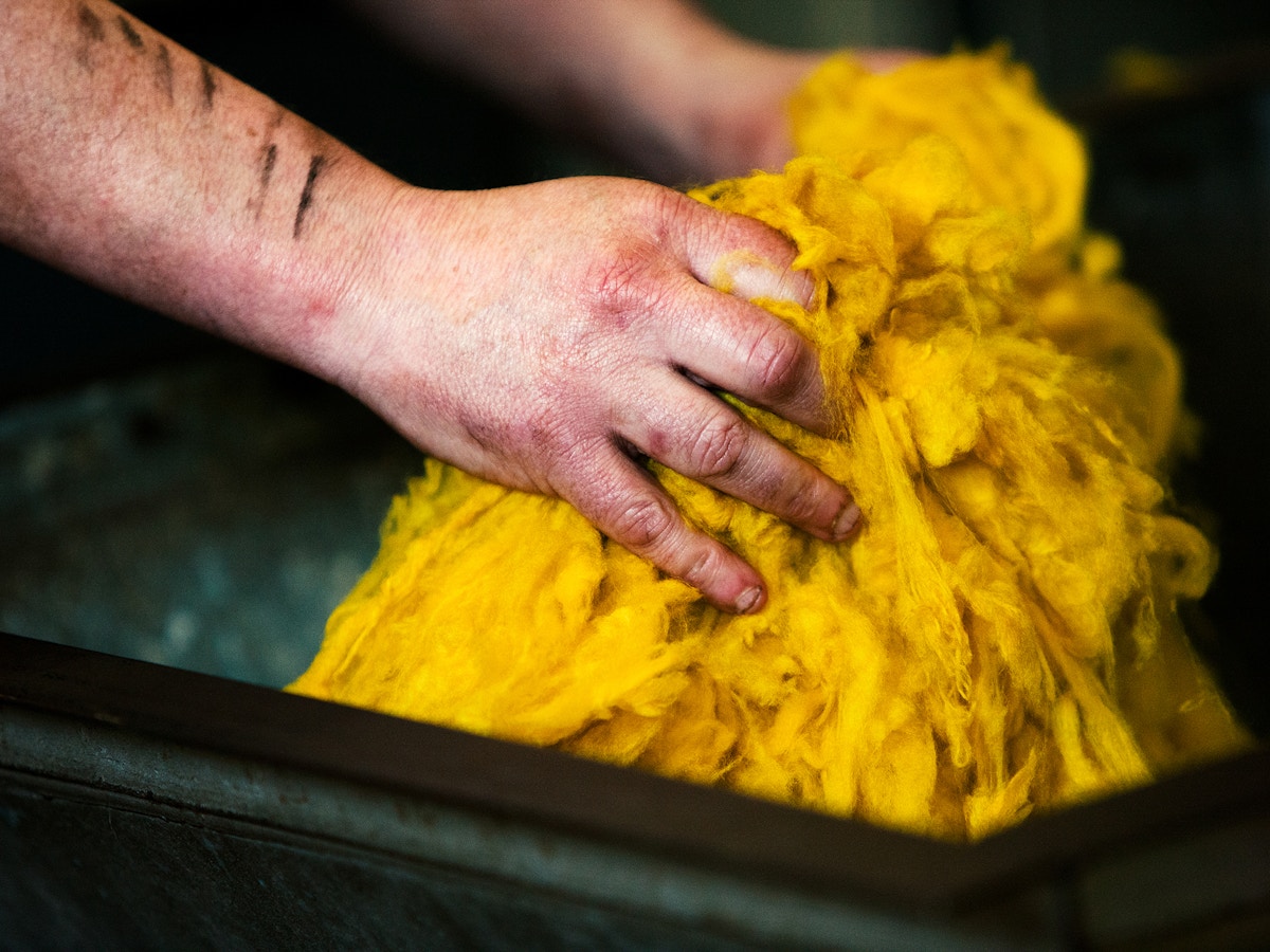 Two hands grasping onto a bright yellow bundle of cashmere.
